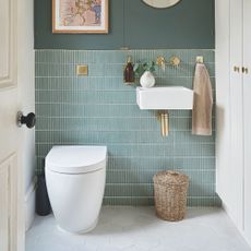 Blue tiled bathroom with grey tiled floor, a white toilet and a white sink with a bin underneath it