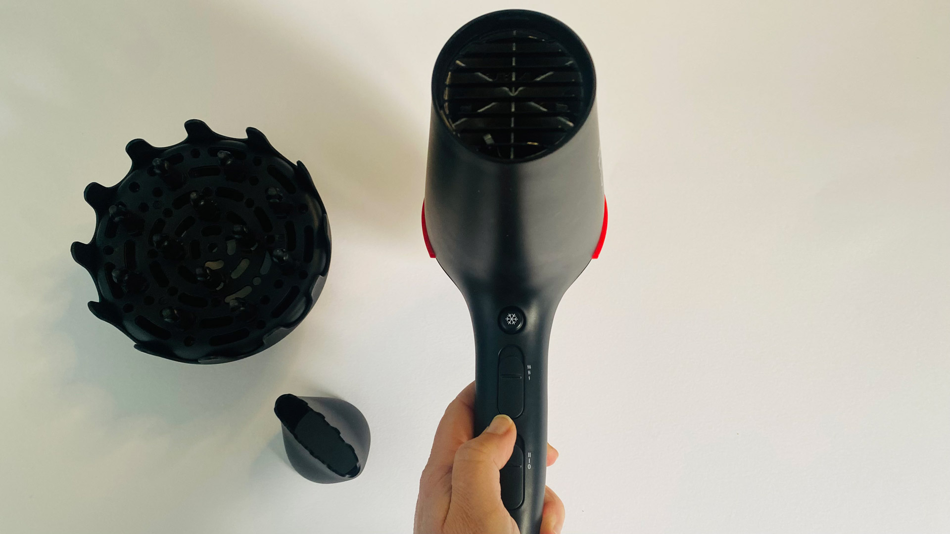 A hand holding the Revlon SmoothStay Coconut-Oil Infused Hair Dryer with accessories on show