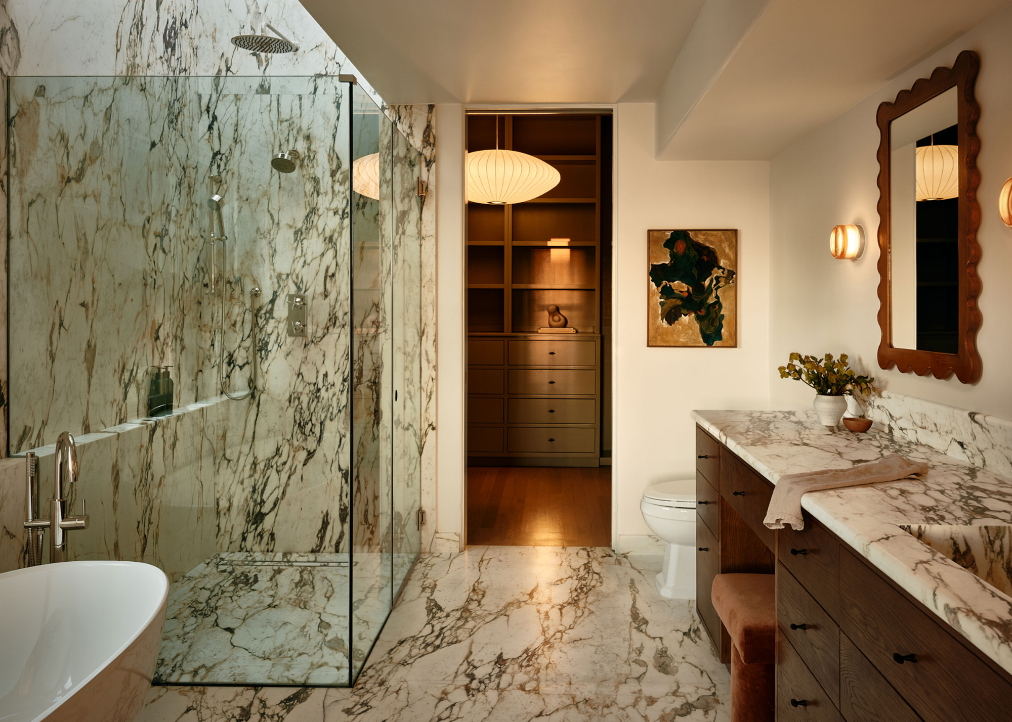 a white marble bathroom with the lights on. The floor and walls and counters are all in the same marble