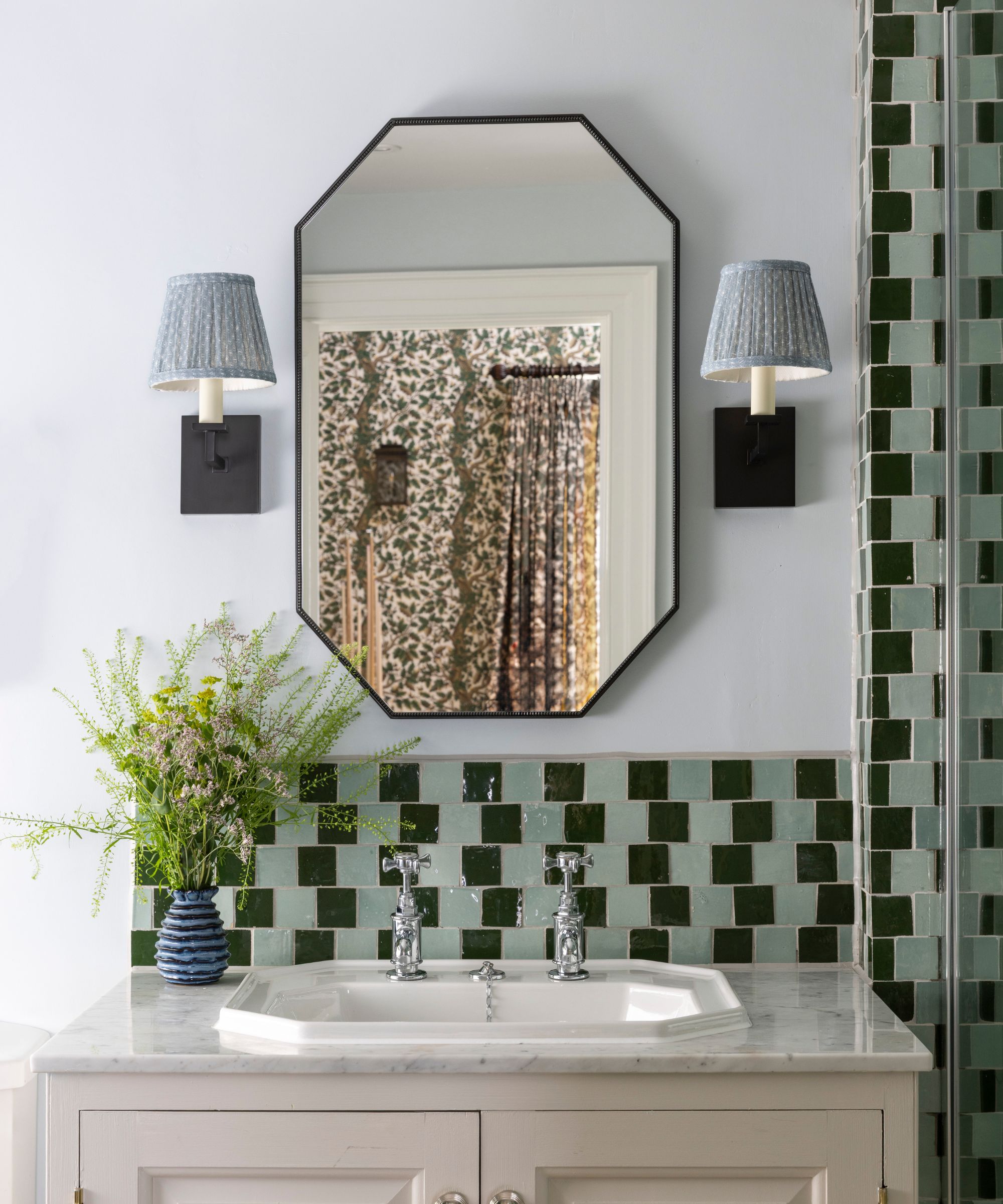 A small bathroom with white walls, a beige vanity, and patterned tiles for the backsplash and shower
