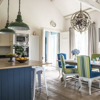 dining area with white walls and wooden dining table with blue chairs and wooden kitchen counter
