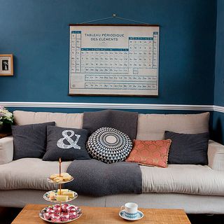 living room with blue wall cream colour and grey sofa with cushion and white chart on wall