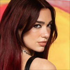 Dua Lipa with red hair in front of a backdrop