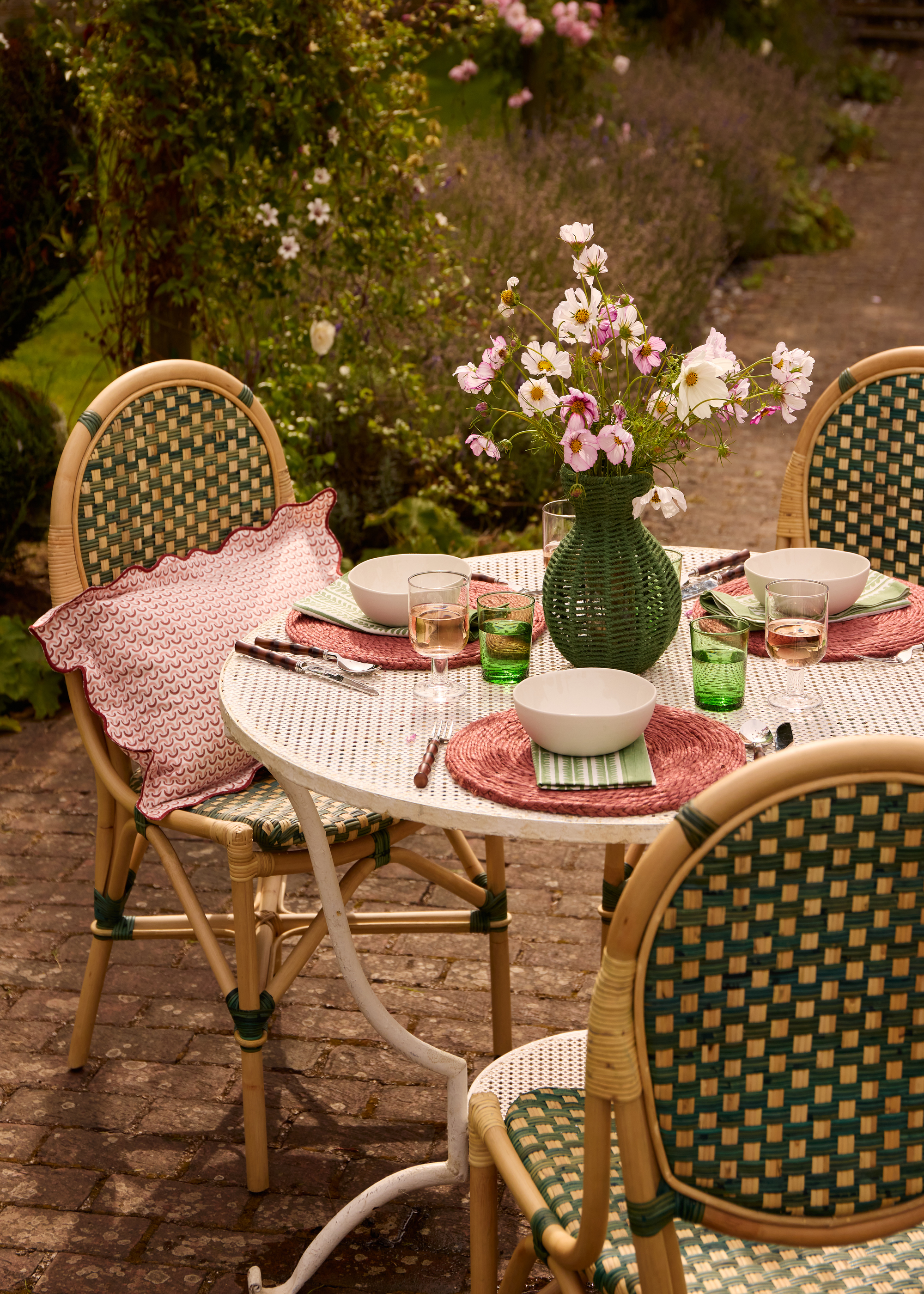 A circular outdoor table laid for dinner with pink placemats, bowls, and a vase of flowers