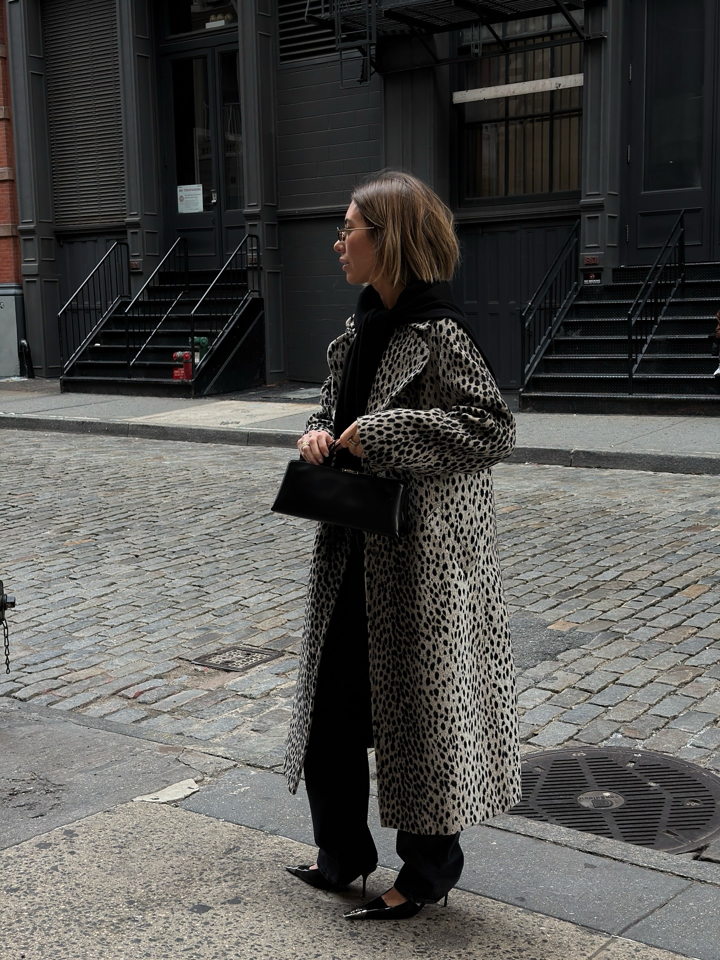 Influencer wears a leopard print coat, black scarf, trousers, and kitten-heels.