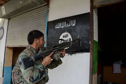 An Afghan soldier puts his gun against the ISIS flag.