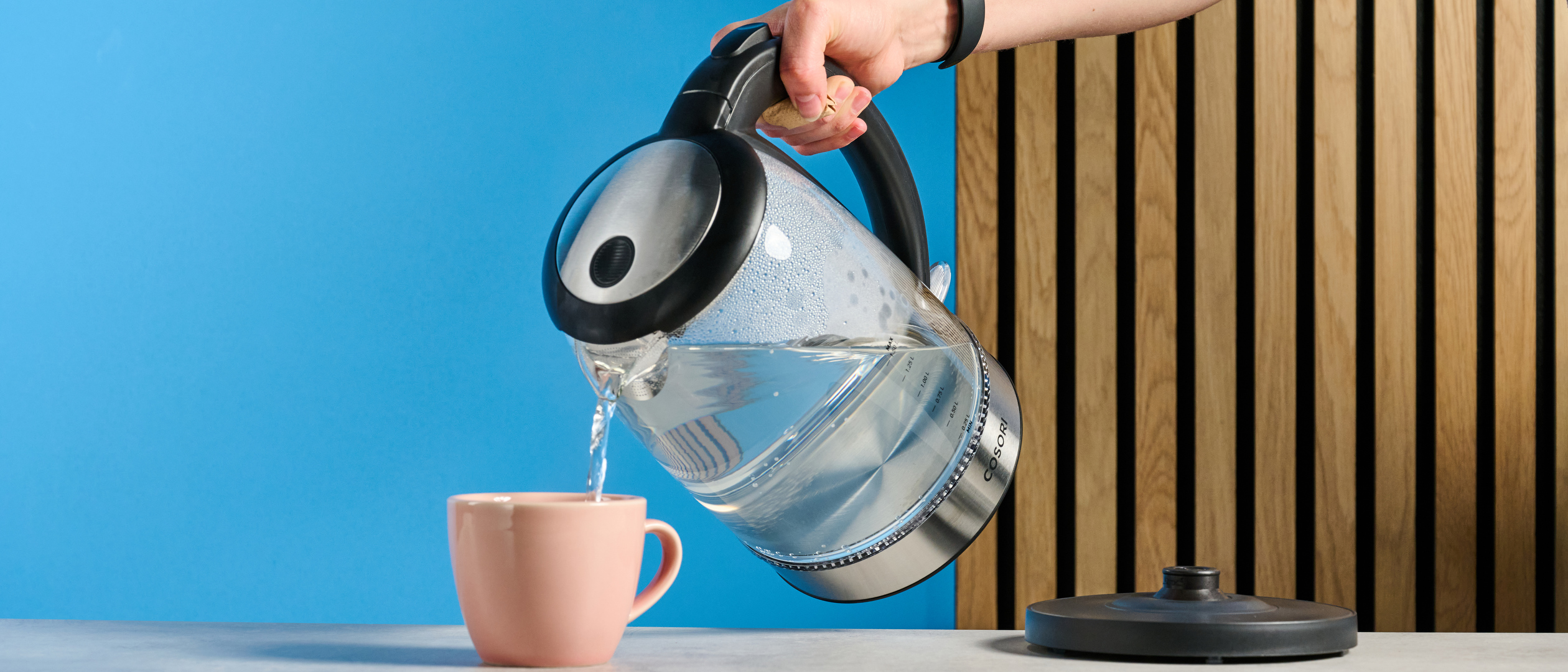 Cosori Electric Glass Kettle photographed in front of a blue background.