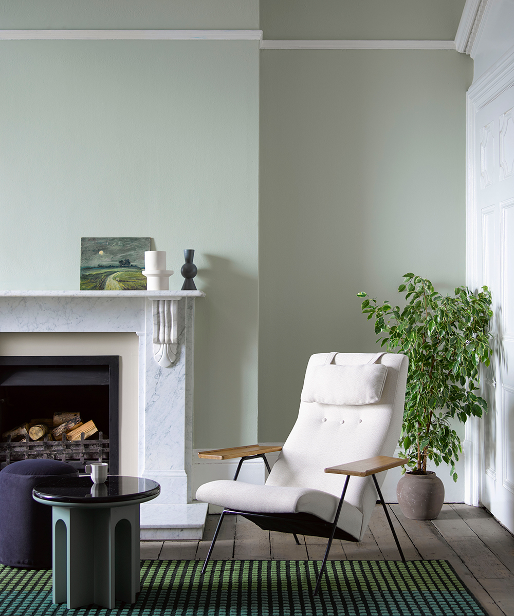 A pale green sofa with cream armchair and modern side table set against a fireplace