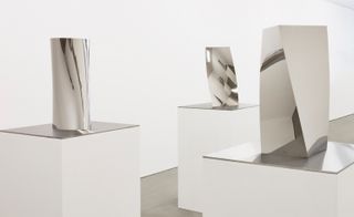 Installation view of ’Gathering Clouds’ at Kukje Gallery. Three rectangular vertical platforms with mirrored tops and a silver object of different shapes on each of them.