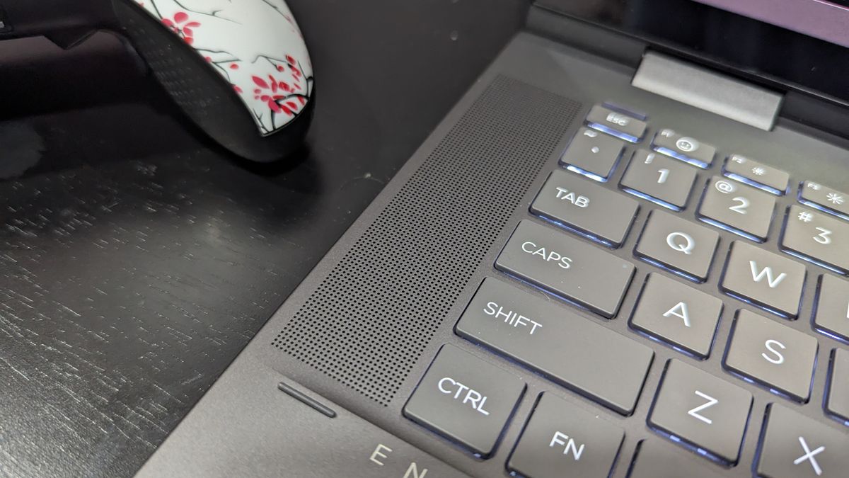 A close up of the speaker grille to the left of a laptop keyboard.