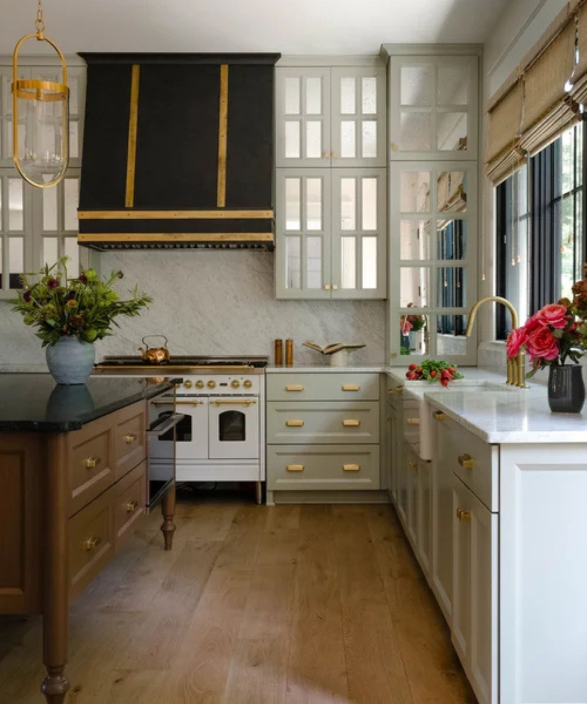 A traditional kitchen with pastel green cabinets, a wooden island, and mirrored panels in the upper cabinets