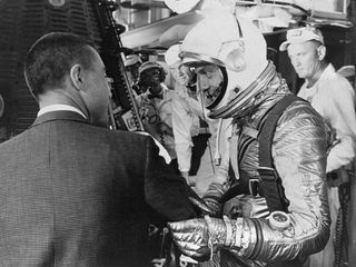 Fellow Mercury astronaut Gus Grissom (in suit) wishes Shepard good luck as he gets set to climb into his Mercury capsule, dubbed Freedom 7, on the morning of May 5, 1961. Glenn looks on in the background.