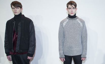 Two male models stood a couple of feet apart, one looking away the other looking directly at the camera
