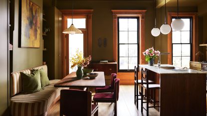An olive green kitchen with a wood island and a striped banquette seating area