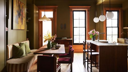 An olive green kitchen with a wood island and a striped banquette seating area