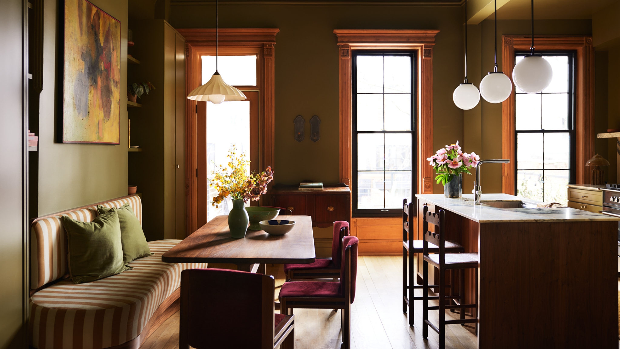 An olive green kitchen with a wood island and a striped banquette seating area
