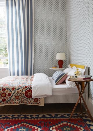bedroom with blue wallpaper, blue stripe curtains, red lamp, patterned rug and bedspread