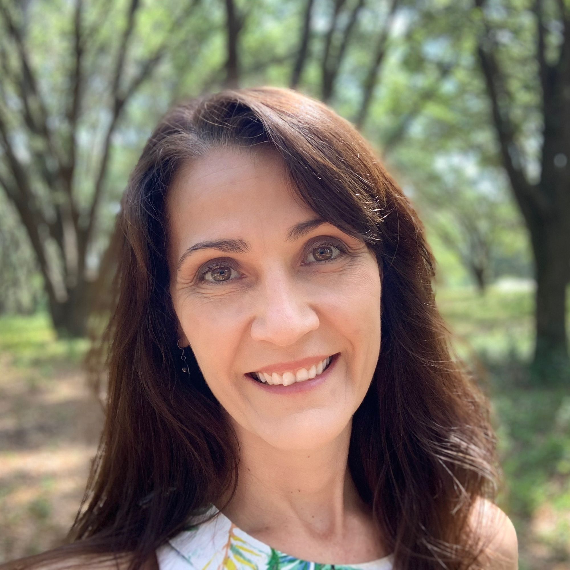 A headshot of Jennifer Pressimone with a blurred forest landscape behind.