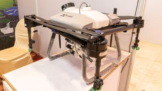 A white drone with four propellors and two stands on a white display table. 