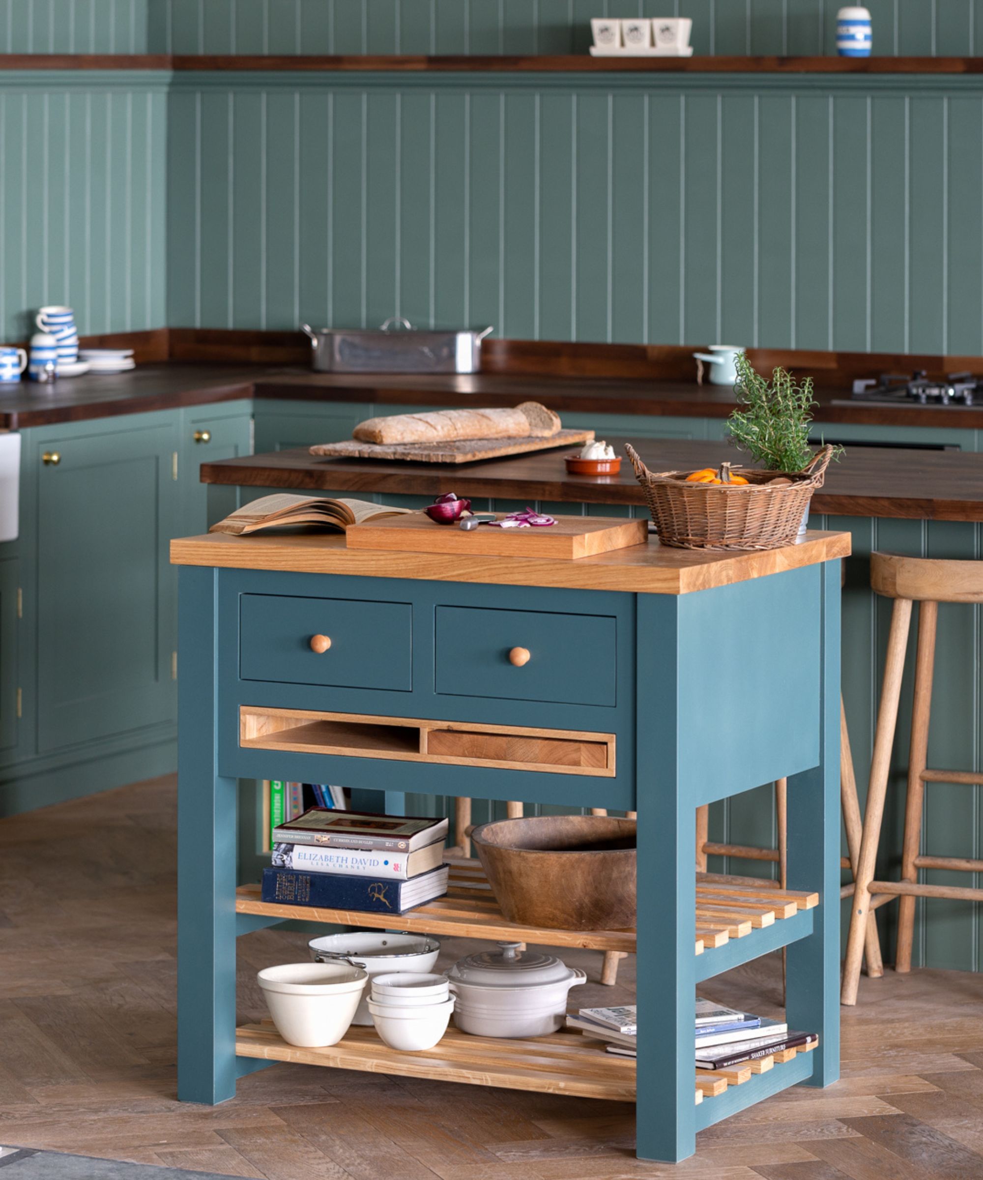 A compact freestanding kitchen island in blue-green tones, with a wooden worktop, open shelving and drawer storage, styled as a flexible prep and storage piece.