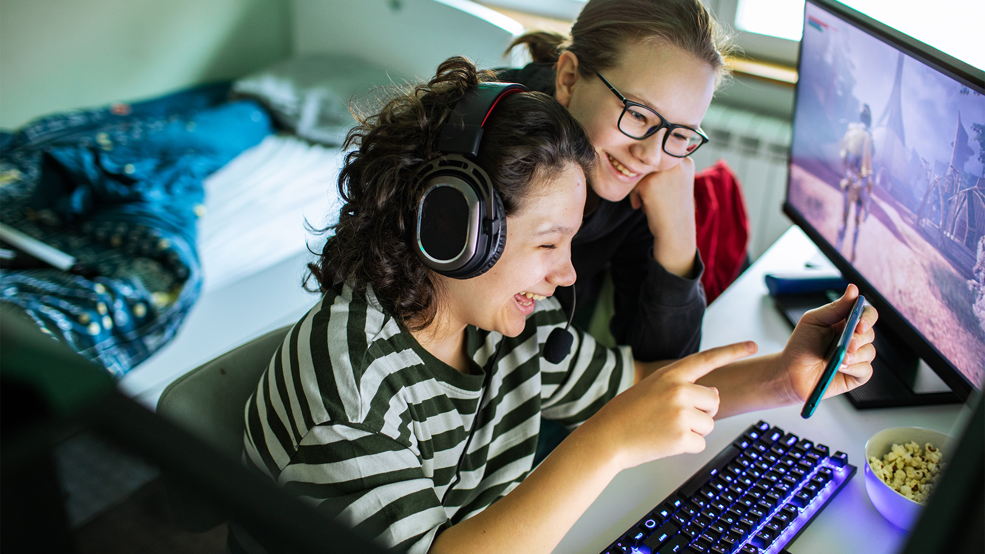 Close up of a Young boy and girl using a smart phone in the bedroom while the boy is playing video games on his computer