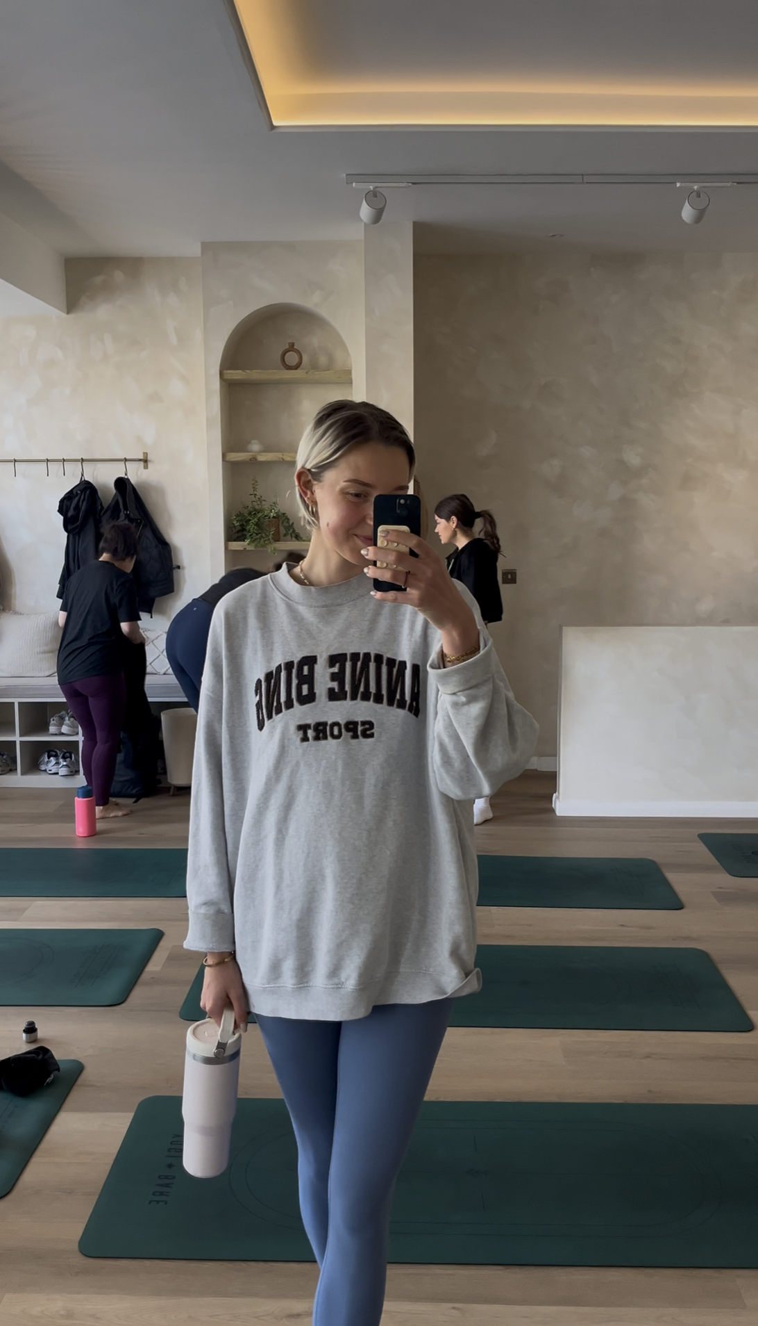 A woman taking a mirror selfie in a yoga studio