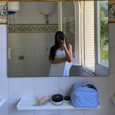 A woman wearing a bath towel and taking a mirror selfie