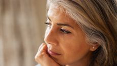 Close-up of a mature, thoughtful woman, resting her chin in her hand and looking away from the camera.