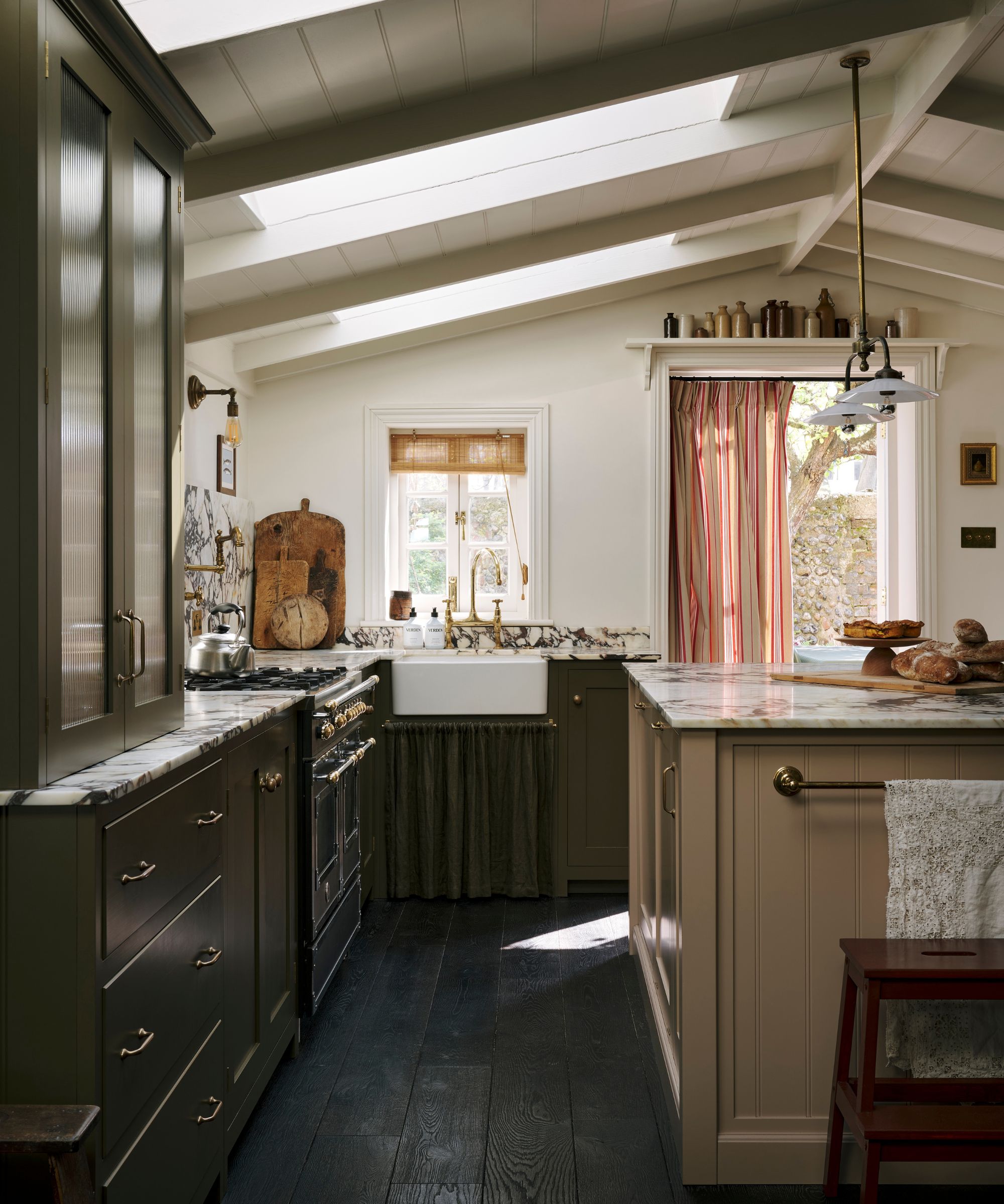 A large kitchen with olive green cabinets, a beige island, marble countertops, and a mix of open and closed storage