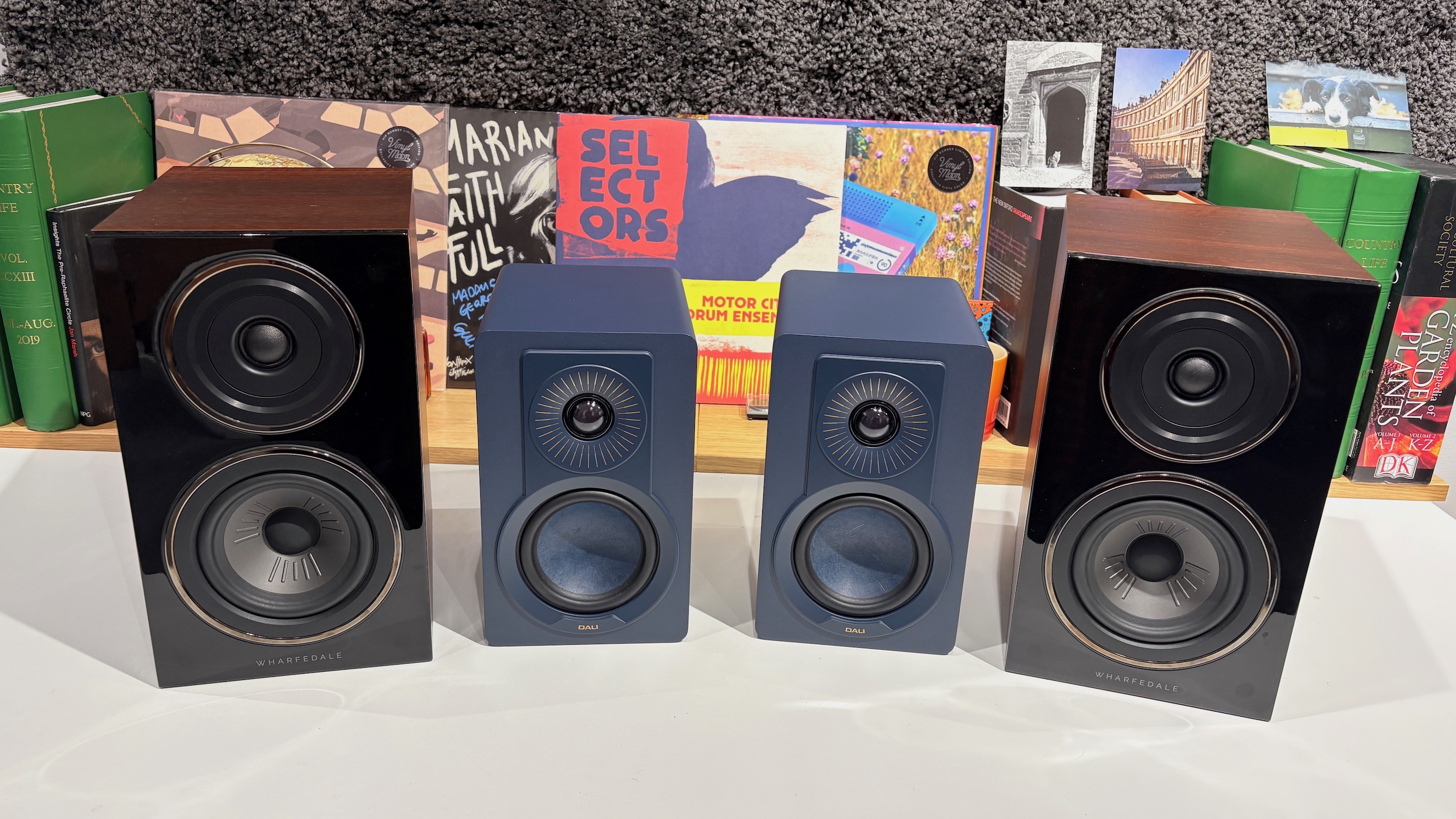 A pair of Dali Kupid and Wharfedale Diamond 12.1 speakers in front of a row of vinyl album covers.