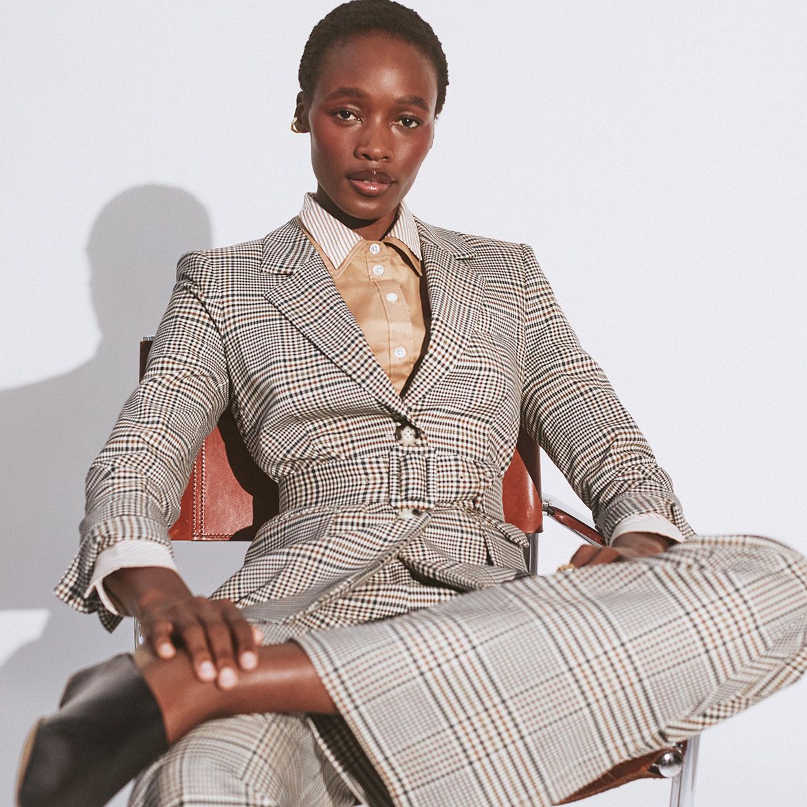 Woman wearing The Outnet checkered tailored suit, sat down with grey background.