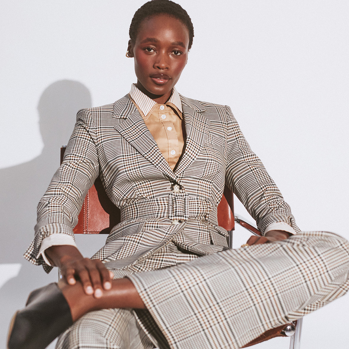 Woman wearing The Outnet checkered tailored suit, sat down with grey background.