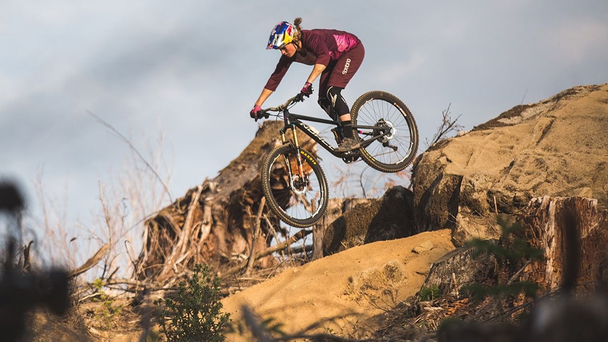 A female rider doing a big drop onto rocks