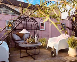 A pale pink painted fence with black egg chair