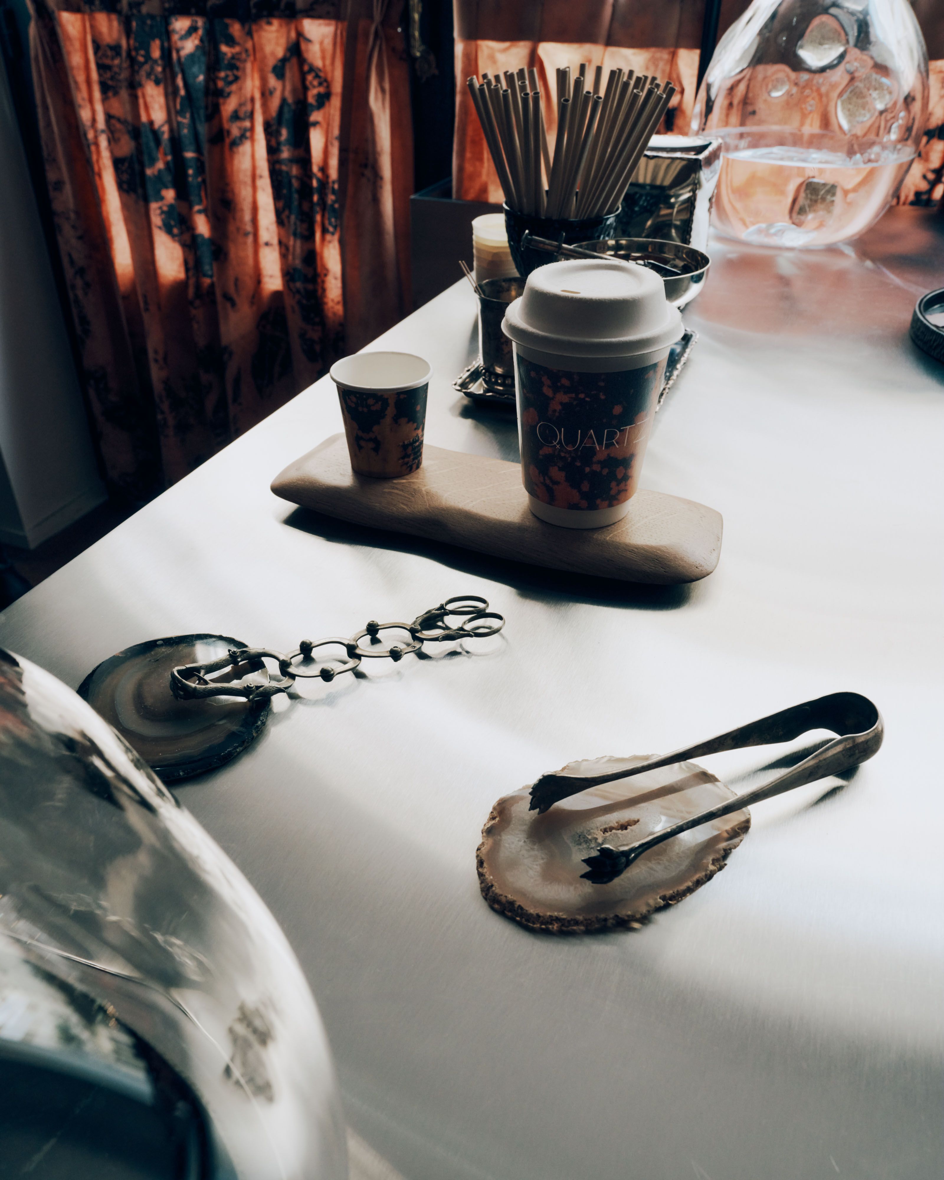 A coffee shop decorated with reflective, organically shaped chrome decor, brown curtains and wooden panels, and ceramic plates.