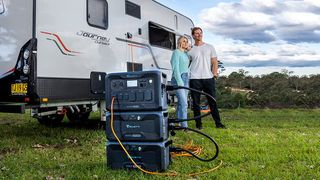 A man and woman stand outside their campervan charging with BLUETTI tech