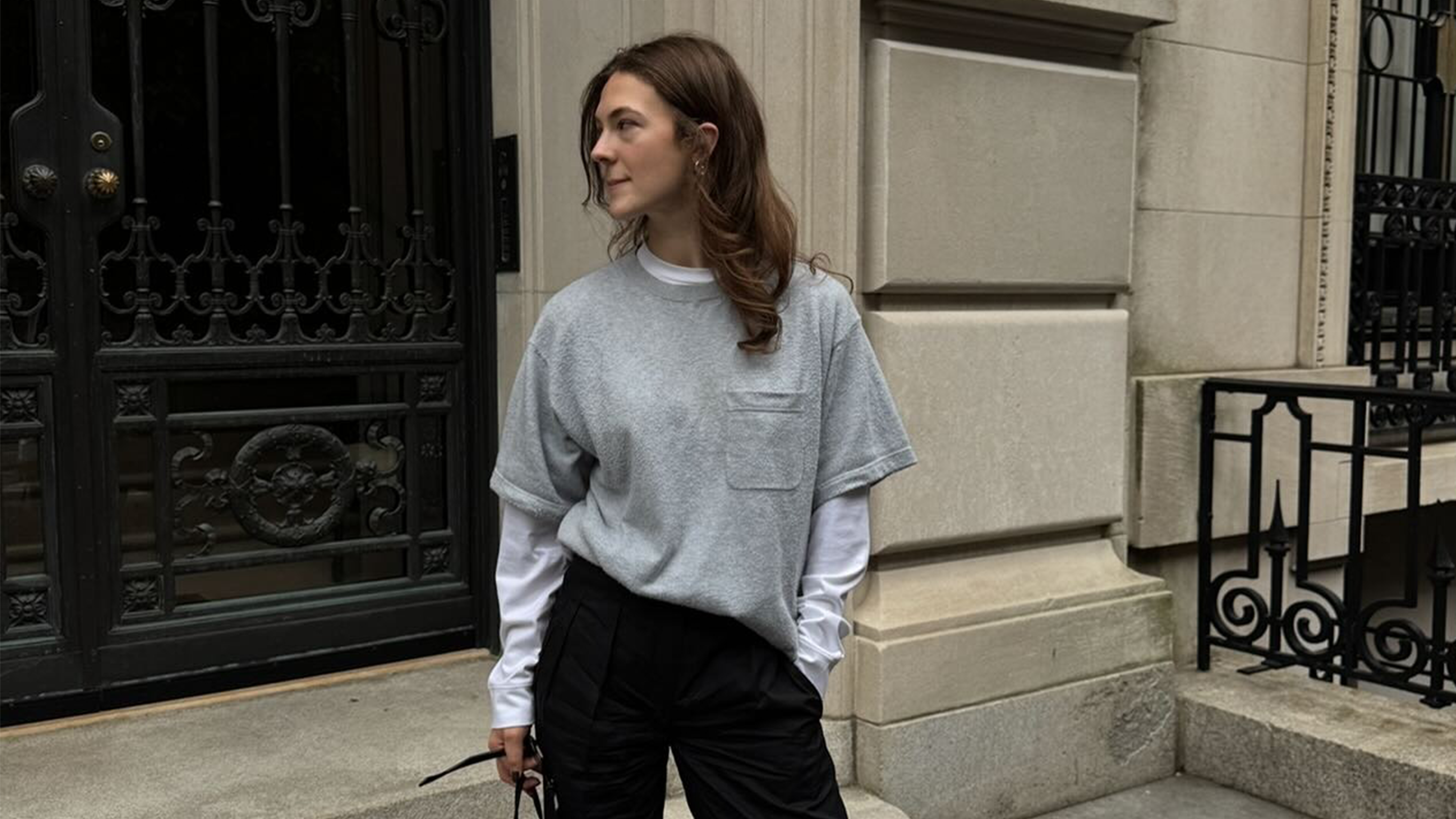Woman wearing a gray T-shirt layered over a white long-sleeve top and black trousers.
