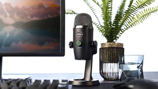 Blue Yeti Nano press shot shoing mic on a desktop next to a monitor screen and a green plant