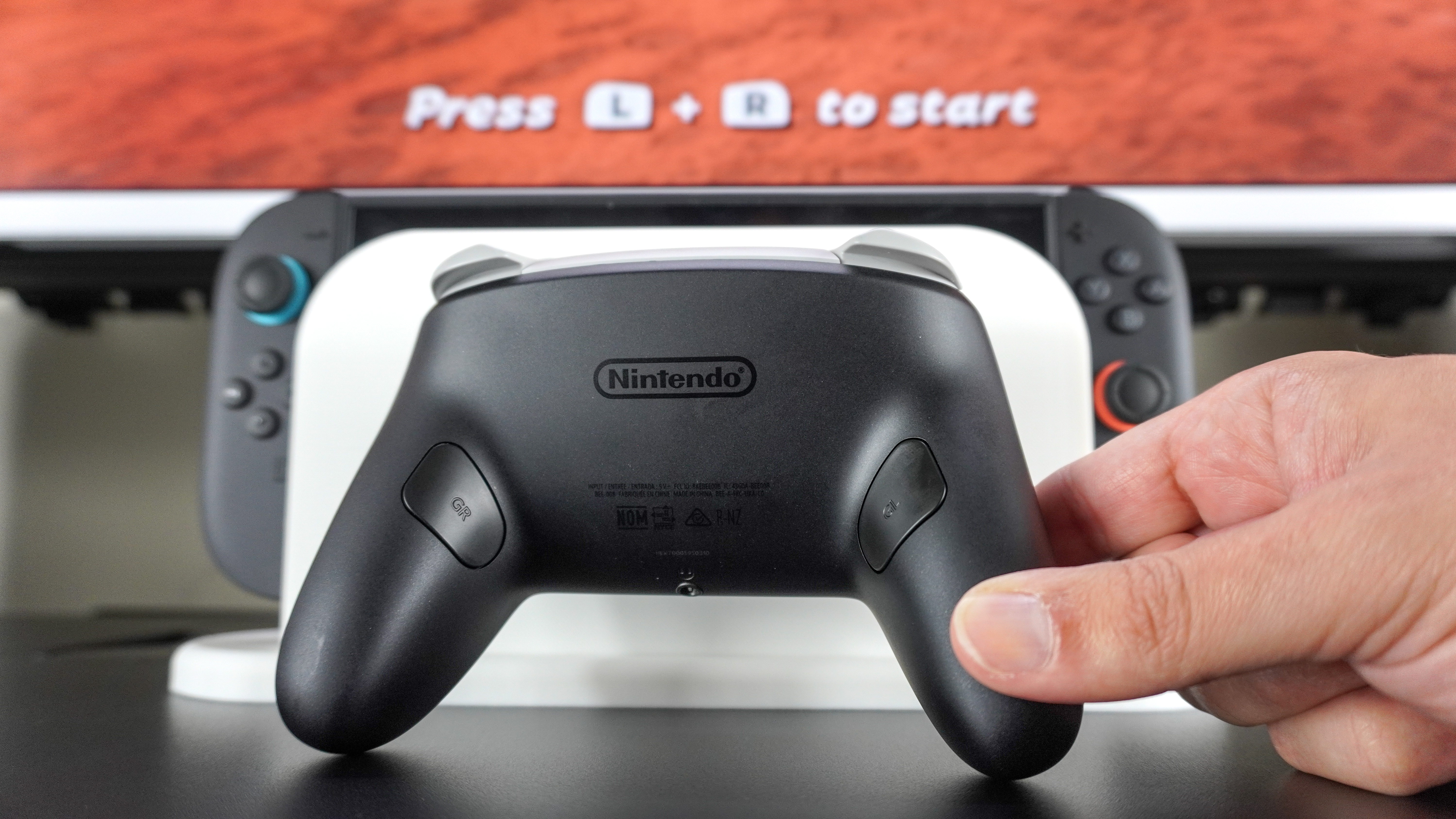 A Nintendo Switch 2 Pro Controller in front of a docked Switch 2 with a game opened on the monitor behind it