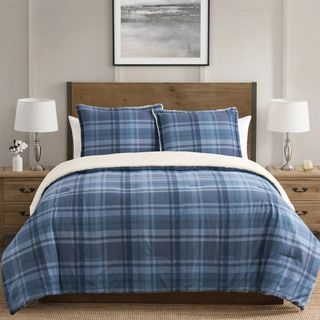 A blue plaid comforter on a wooden bed. 