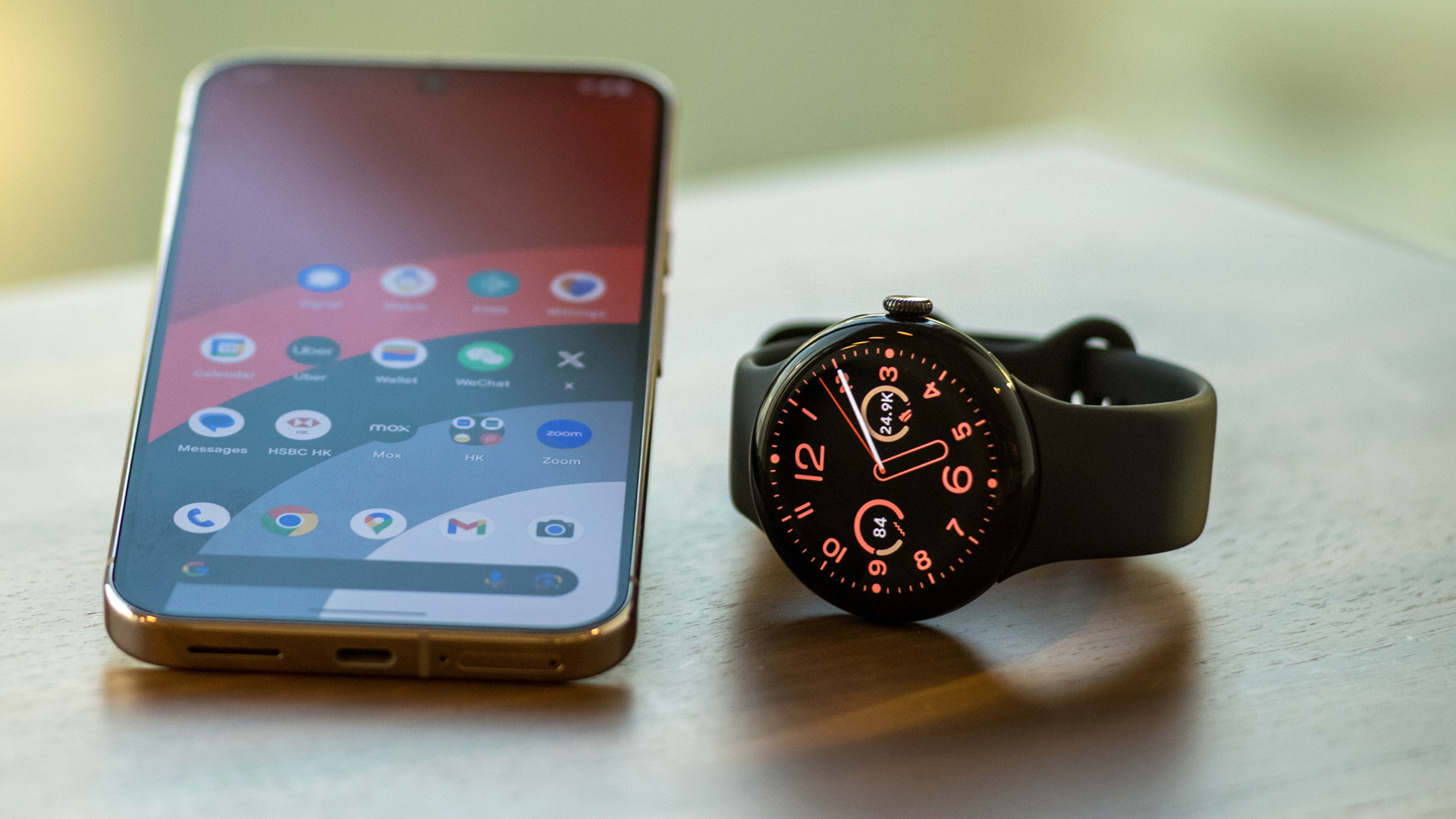 Google Pixel Watch 3 lying on a desktop alongside a Pixel 9 phone
