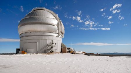 a conical white building with a silver domed roof is seen under a bright blue sky and a snow-covered ground