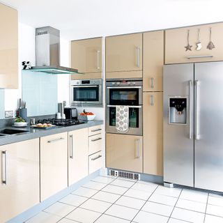 Beige kitchen with grey worktops and white floor tiles and a freestanding stainless steel fridge freezer