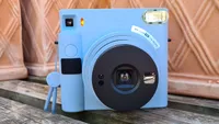 En Fujifilm Instax SQ1 direktbildskamera placerad på en träbänk.