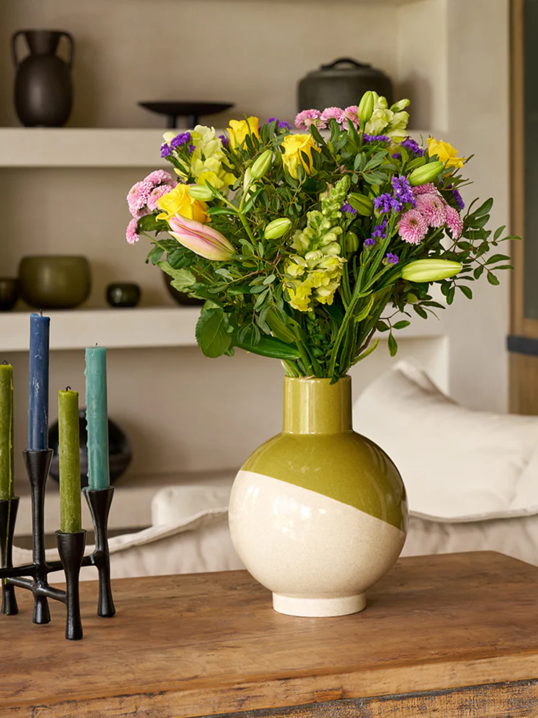 A vase of colorful scented flowers from Arena Flowers on a wood table beside candlesticks