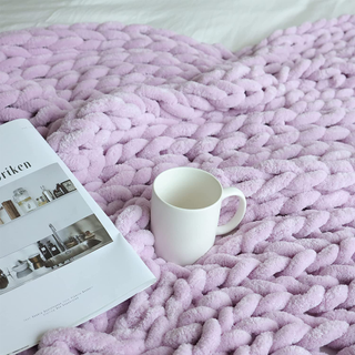 A lavender chunky knit throw blanket with coffee cup and coffee table photo book