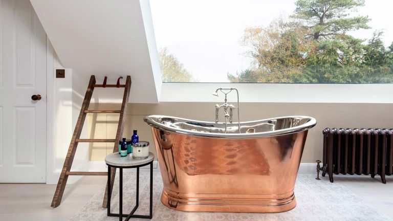 copper roll top bath tub with bath products and ladder in a room with huge window