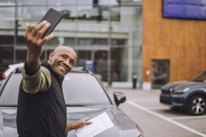 Happy man taking selfie through smart phone after purchasing new car