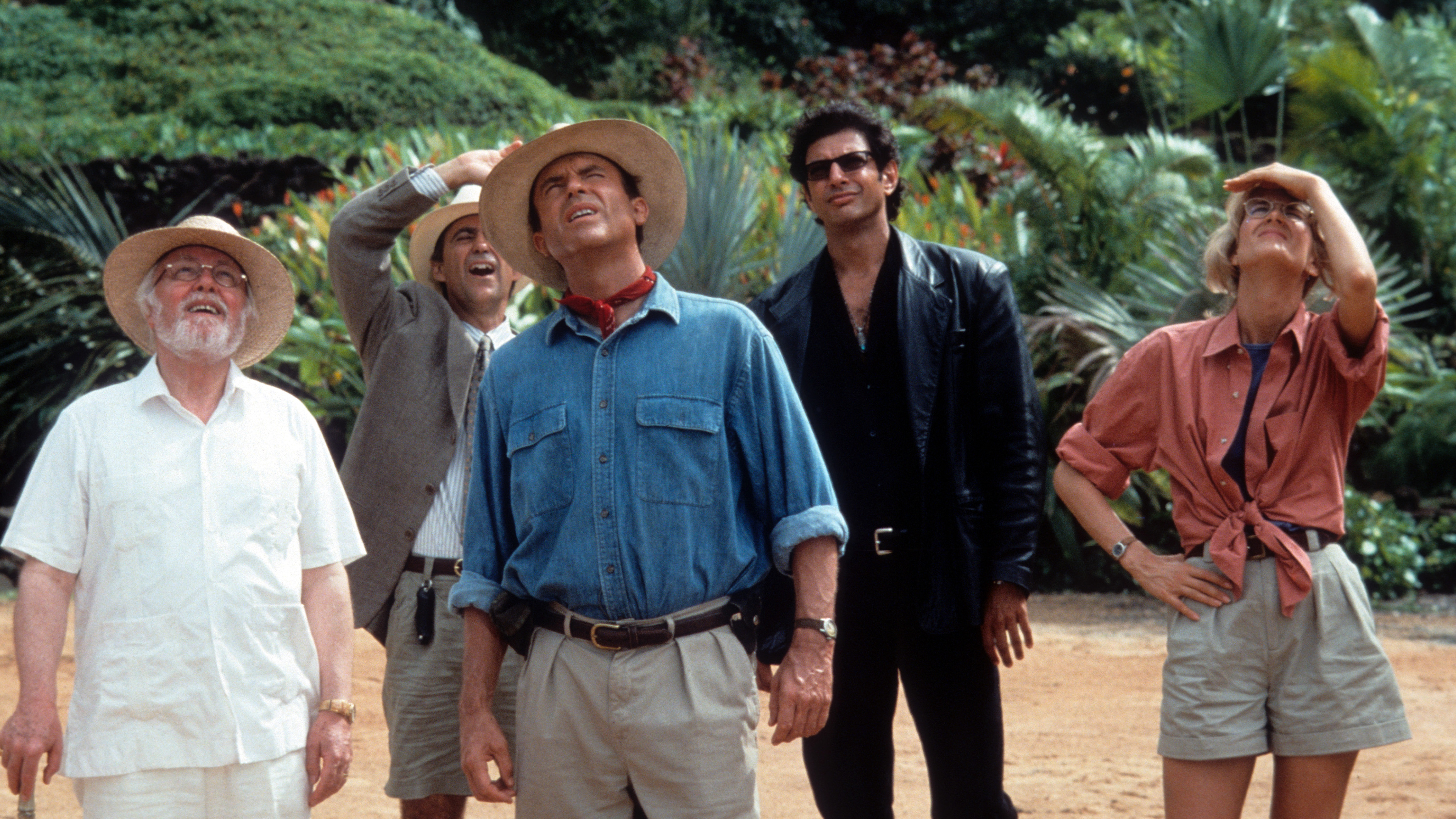 A still from the movie Jurassic Park in which all of the major characters are stood outdoors and looking up at something off camera.