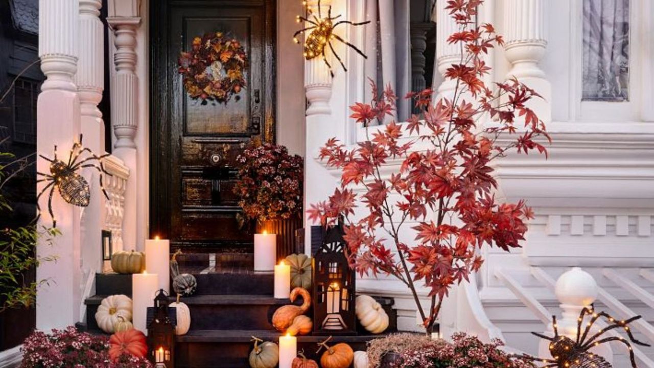 A Halloween wreath on a black front door; pumpkins and spiders on the porch steps.